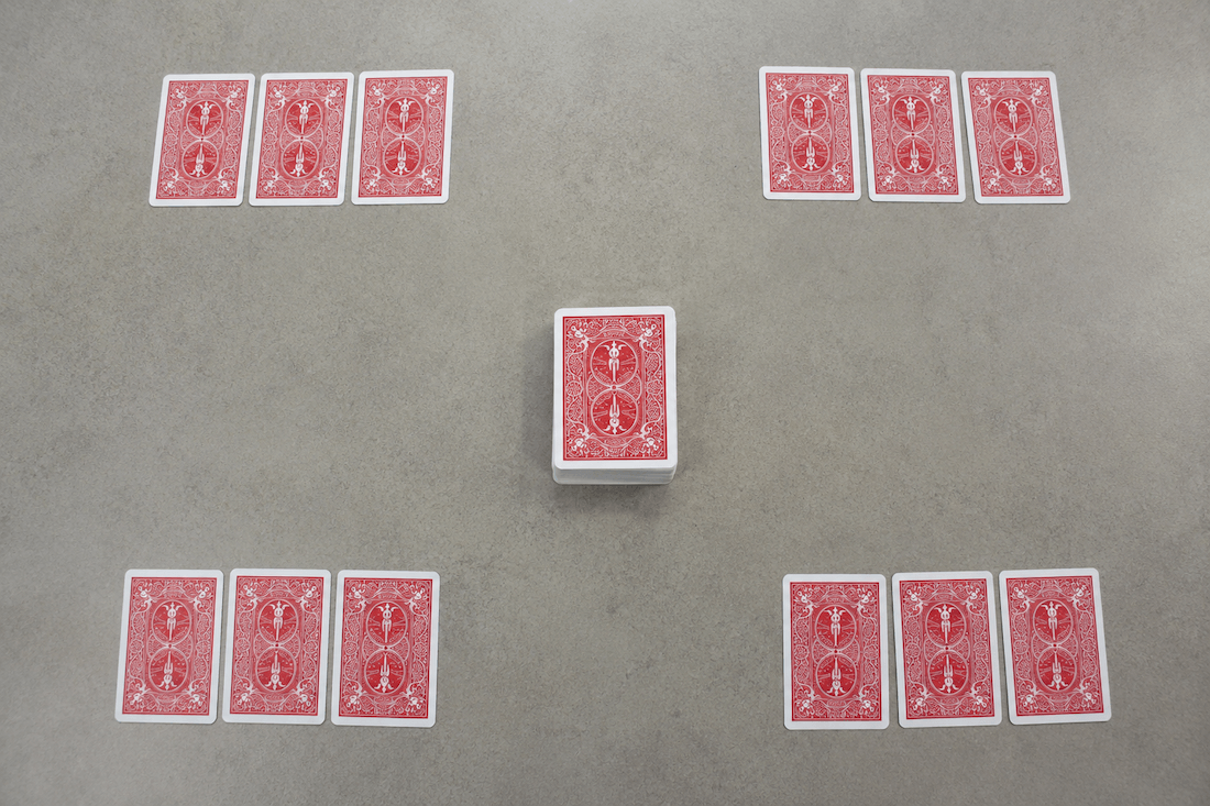 Setup for the Noventa y Nueve Spanish numbers card game, with three cards for each player and the draw pile in the center.